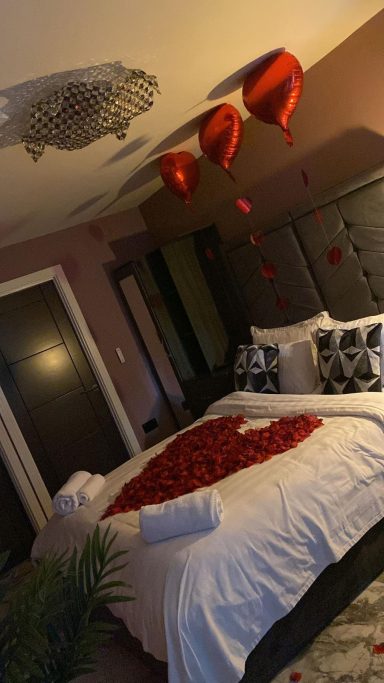 A romantic bedroom with heart-shaped rose petals and red balloons.